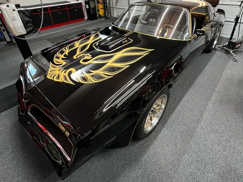 A black Trans Am with a gold hood decal, polished