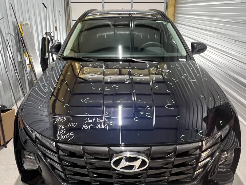 A black Hyundai in the shop with hail dents marked on the hood